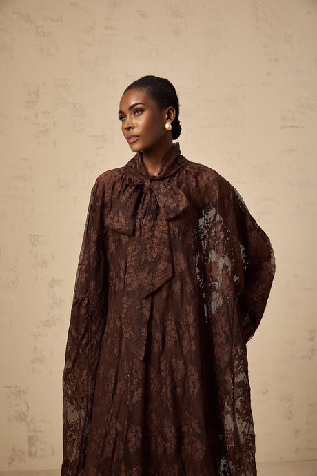 A woman wearing a brown flared midi dress made of chantilly lace with a fitted bodice and flowing skirt