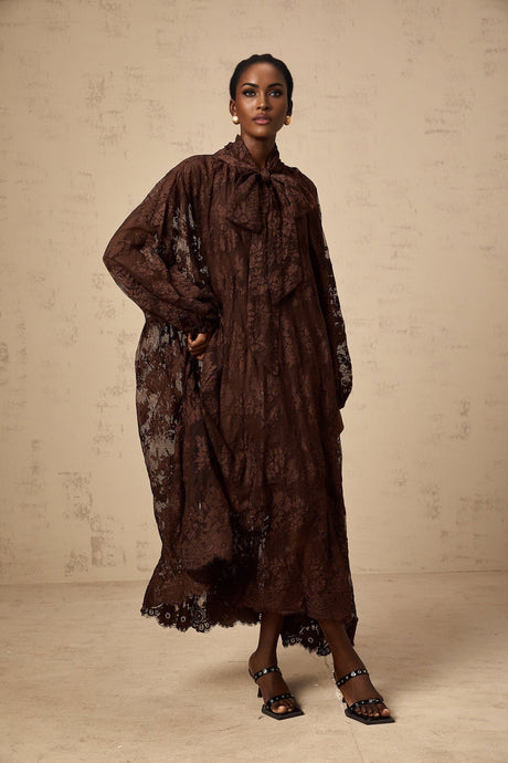 A woman wearing a brown lace midi dress with a flared skirt and delicate chantilly lace pattern The dress has a fitted bodice and falls to mid calf length