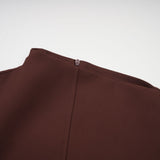 A woman wearing a brown mini dress with an asymmetric neckline and puff sleeves standing against a plain background