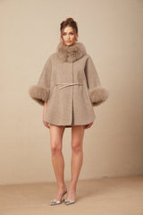 A woman wearing a brown wool cape coat with fur trim and a belt cinching the waist