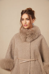 A woman wearing a brown wool cape coat with fur trim and a belt cinching the waist
