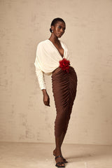 A woman wearing a colorblocked midi dress with a ruched design and a large flower brooch accent The dress features contrasting colors and falls to mid calf length