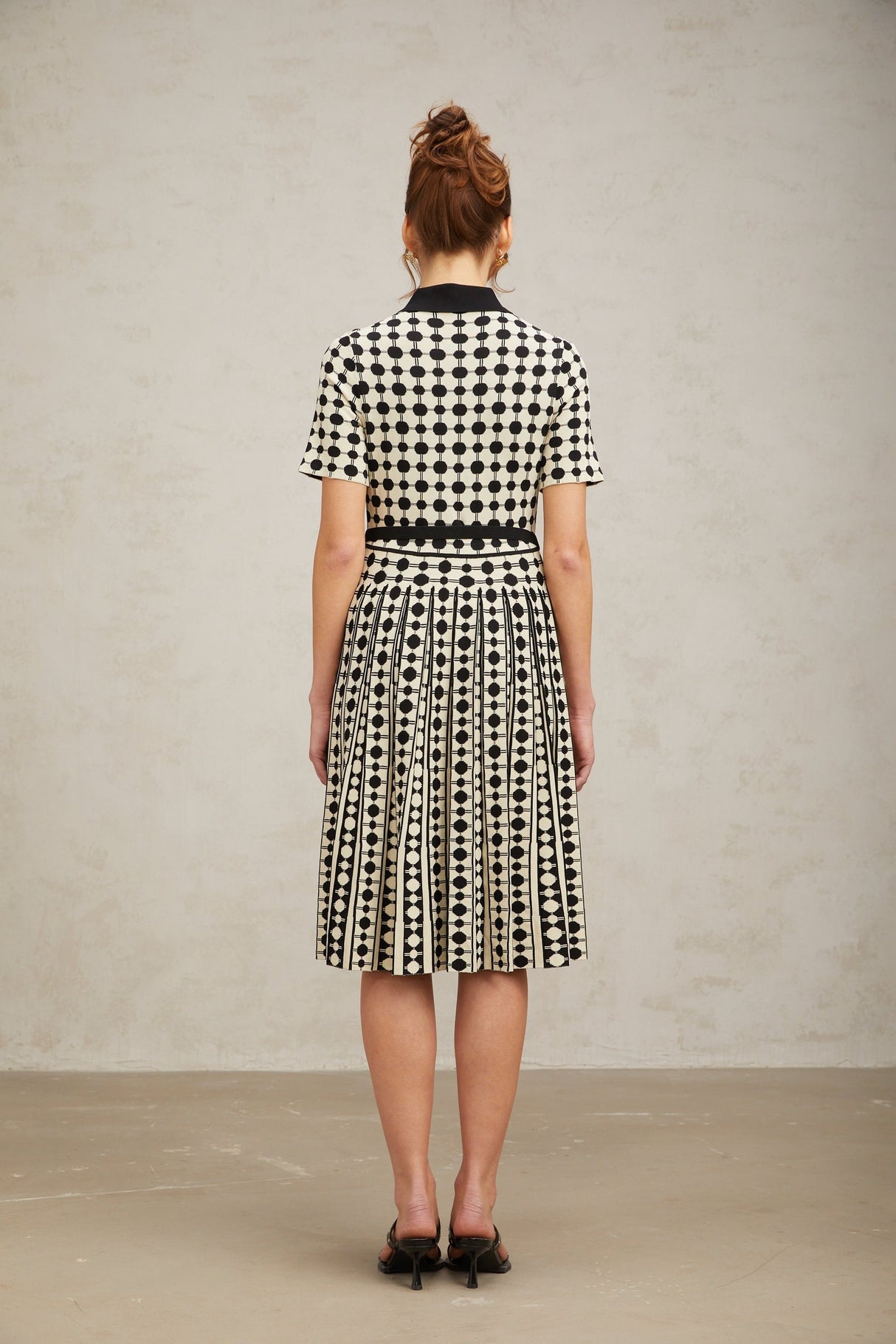 A woman wearing a colorblocked midi dress with polka dot pattern in contrasting colors standing against a plain background