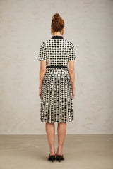 A woman wearing a colorblocked midi dress with polka dot pattern in contrasting colors standing against a plain background