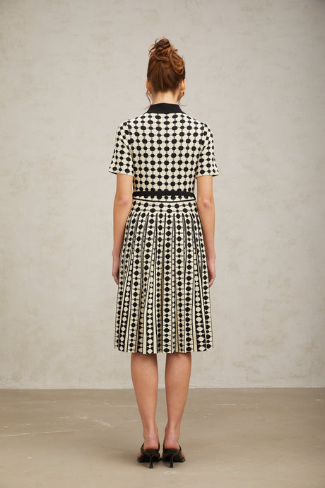 A woman wearing a colorblocked midi dress with polka dot pattern in contrasting colors standing against a plain background