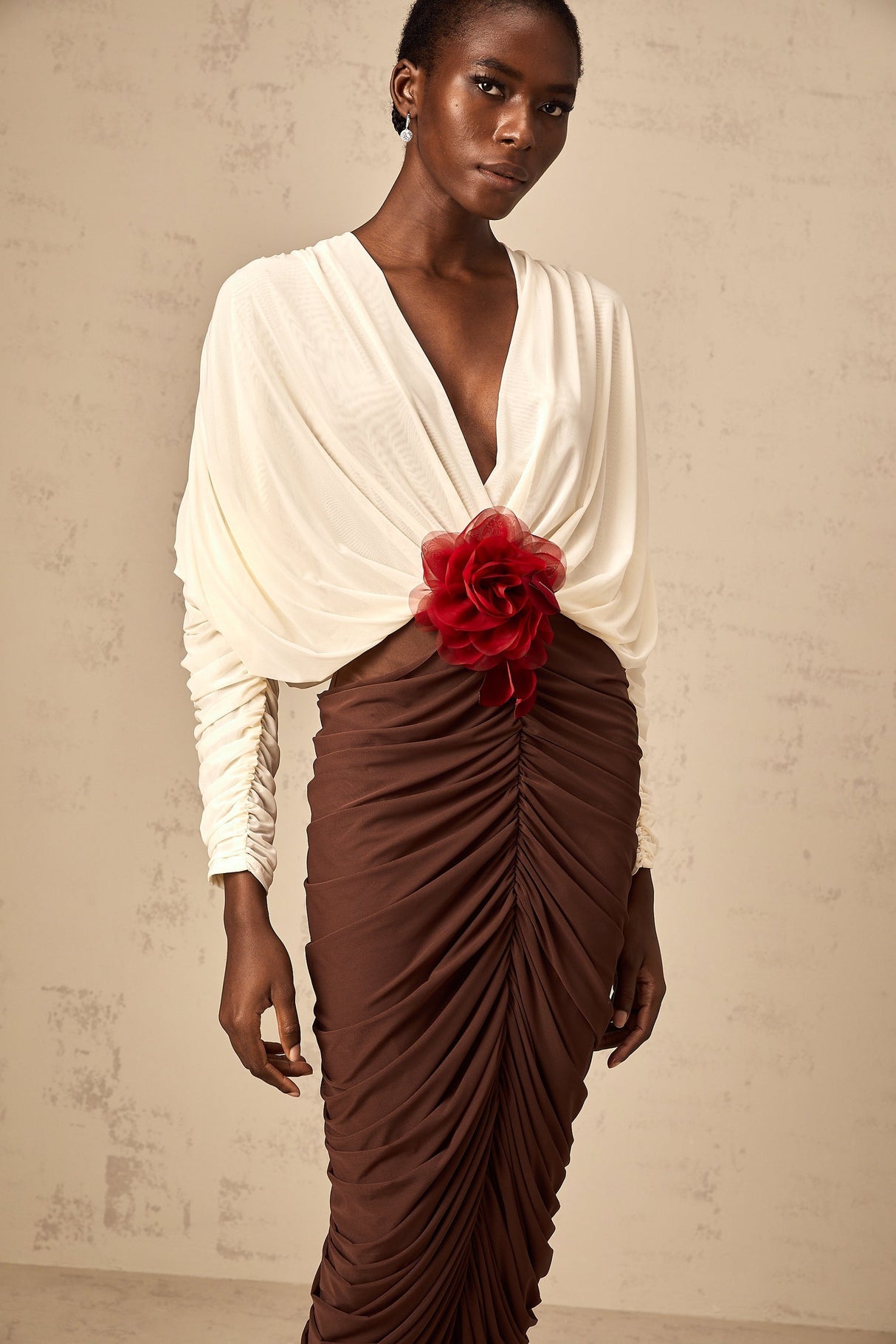 A woman wearing a colorblocked midi dress with ruched detailing and a floral brooch accent The dress features contrasting colors and falls to mid calf length