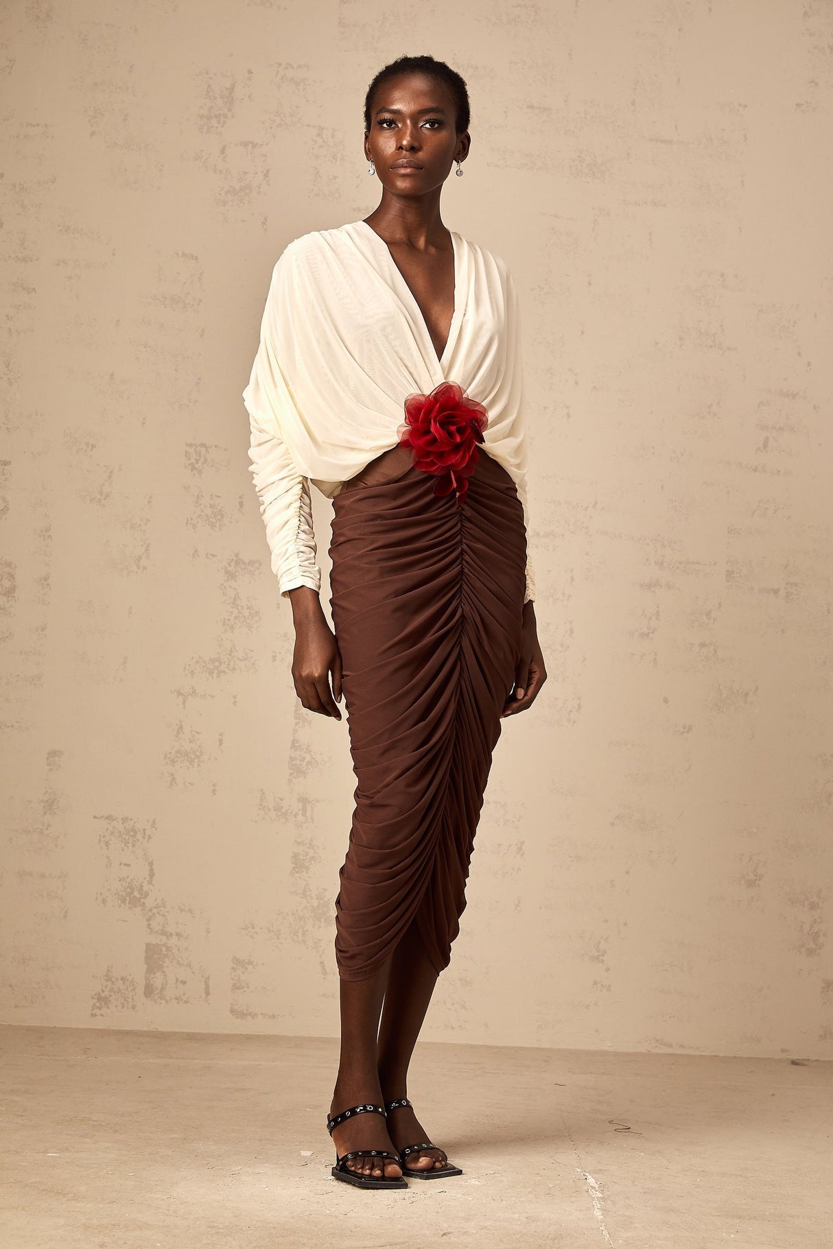 A woman wearing a colorblocked midi dress with ruched detailing and a floral brooch accent The dress features contrasting colors and falls to mid calf length