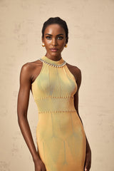 A woman wearing a cream colored knit midi dress with faux pearl embellishments along the neckline and sleeves standing in a neutral background