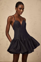 A woman wearing a dark blue denim mini dress with a flounce detail standing against a plain background