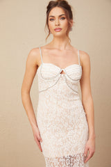 A woman wearing a fitted midi length dress with a crystal embellished bustier top and lace skirt portion The dress is likely in a light or neutral color and has a sleeveless design with a sweetheart neckline
