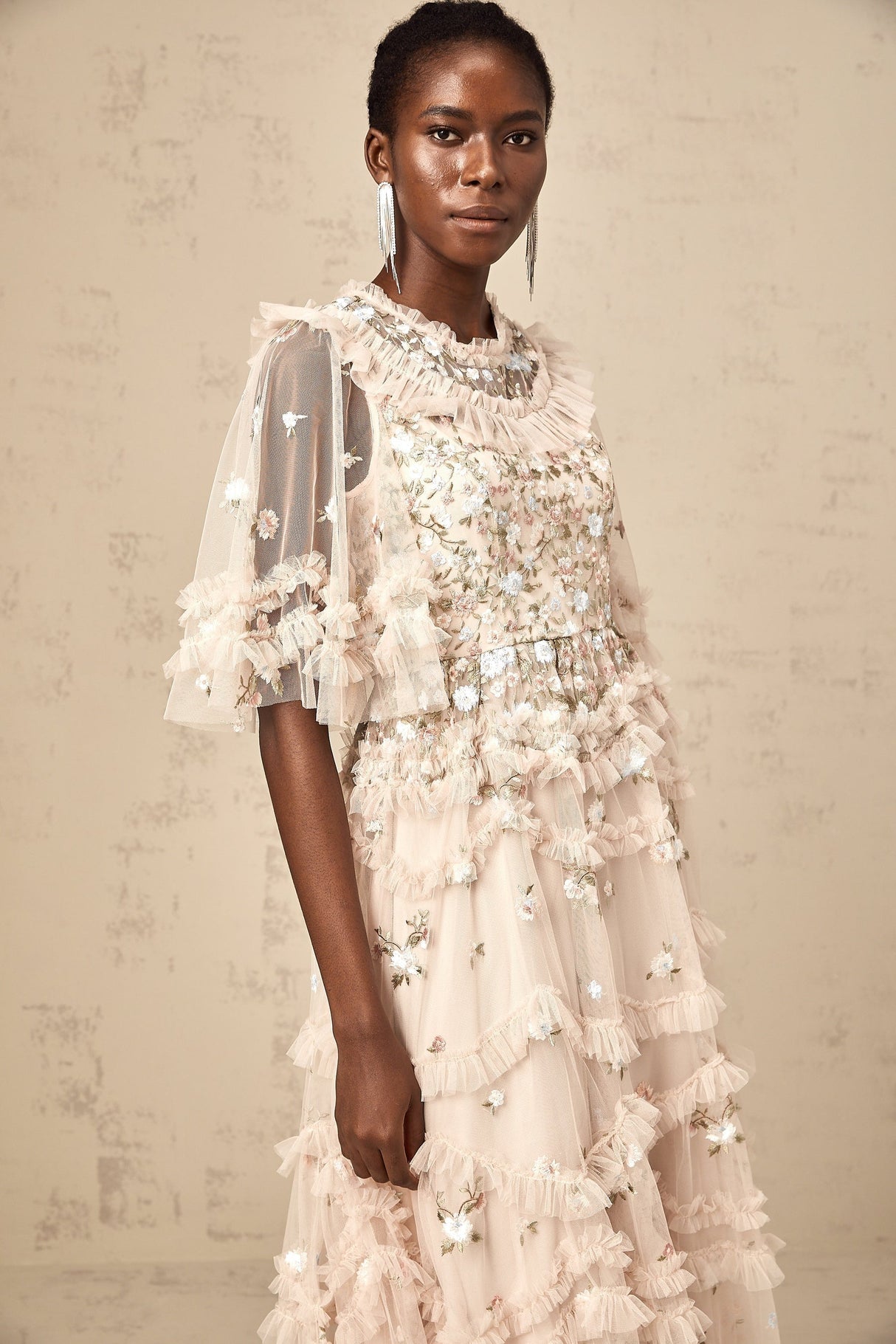 A woman wearing a floral embroidered midi dress with tiered ruffles and a light flowing fabric