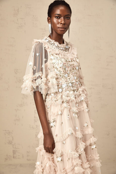 A woman wearing a floral embroidered midi dress with tiered ruffles and a light flowing fabric