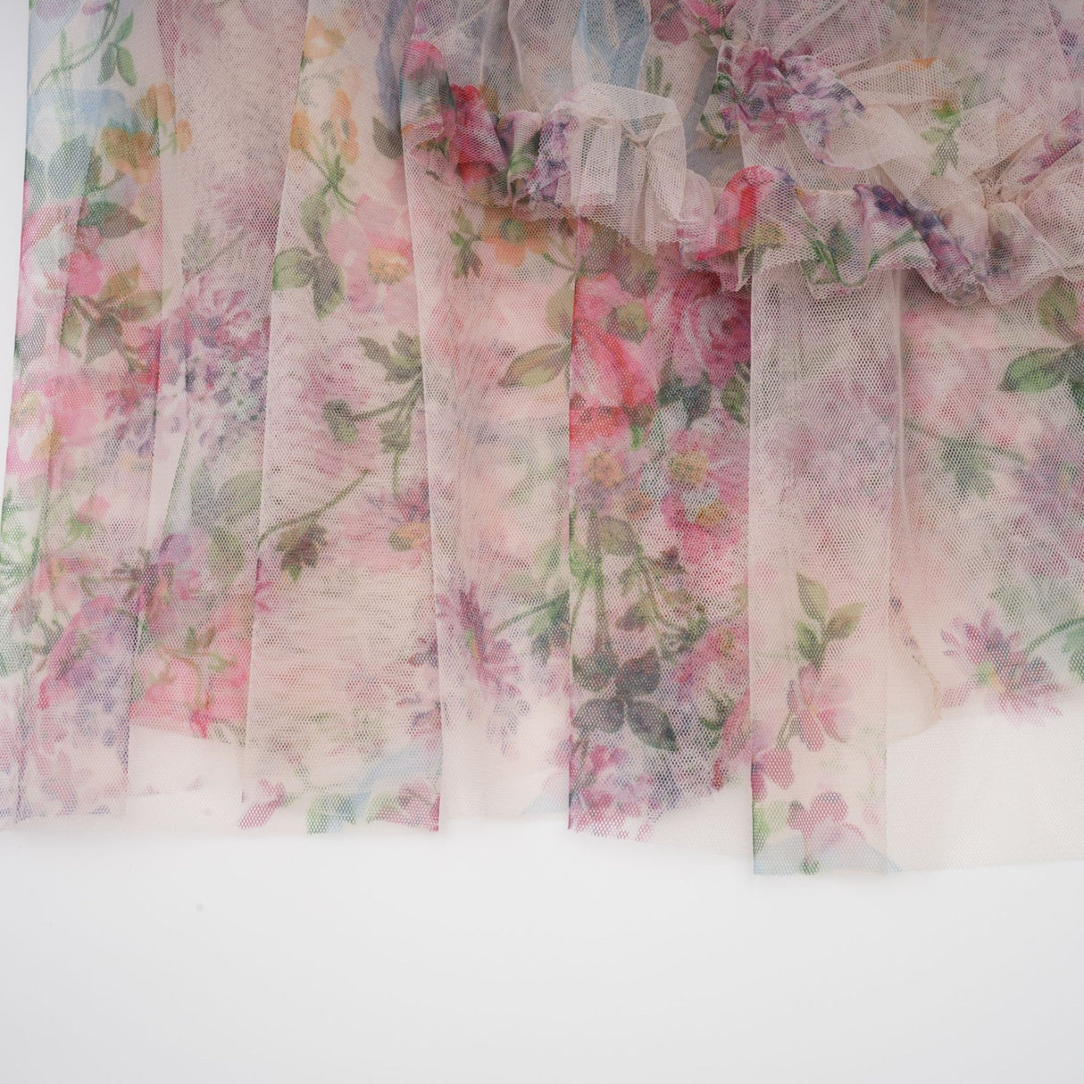 A woman wearing a floral midi dress with ruffled tulle details and a delicate floral pattern standing against a plain background
