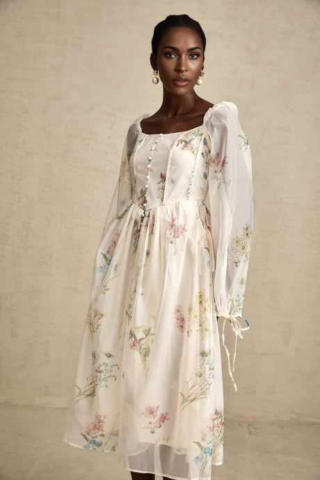 A woman wearing a floral print midi dress with a square neckline and a fitted waist The dress features a colorful floral pattern on a light background and falls to mid calf length