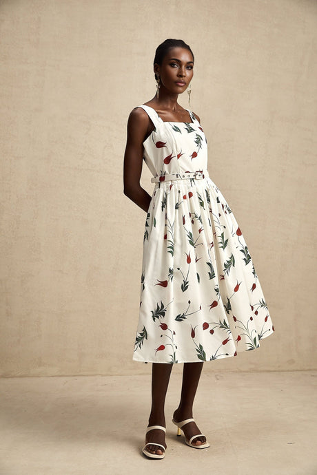 A woman wearing a floral print midi dress with a vibrant pattern standing in a garden setting The dress features short sleeves a fitted waist and a flowing skirt that falls to mid calf length