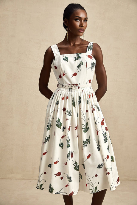 A woman wearing a floral print midi dress with a white background and colorful flower pattern standing in a relaxed pose