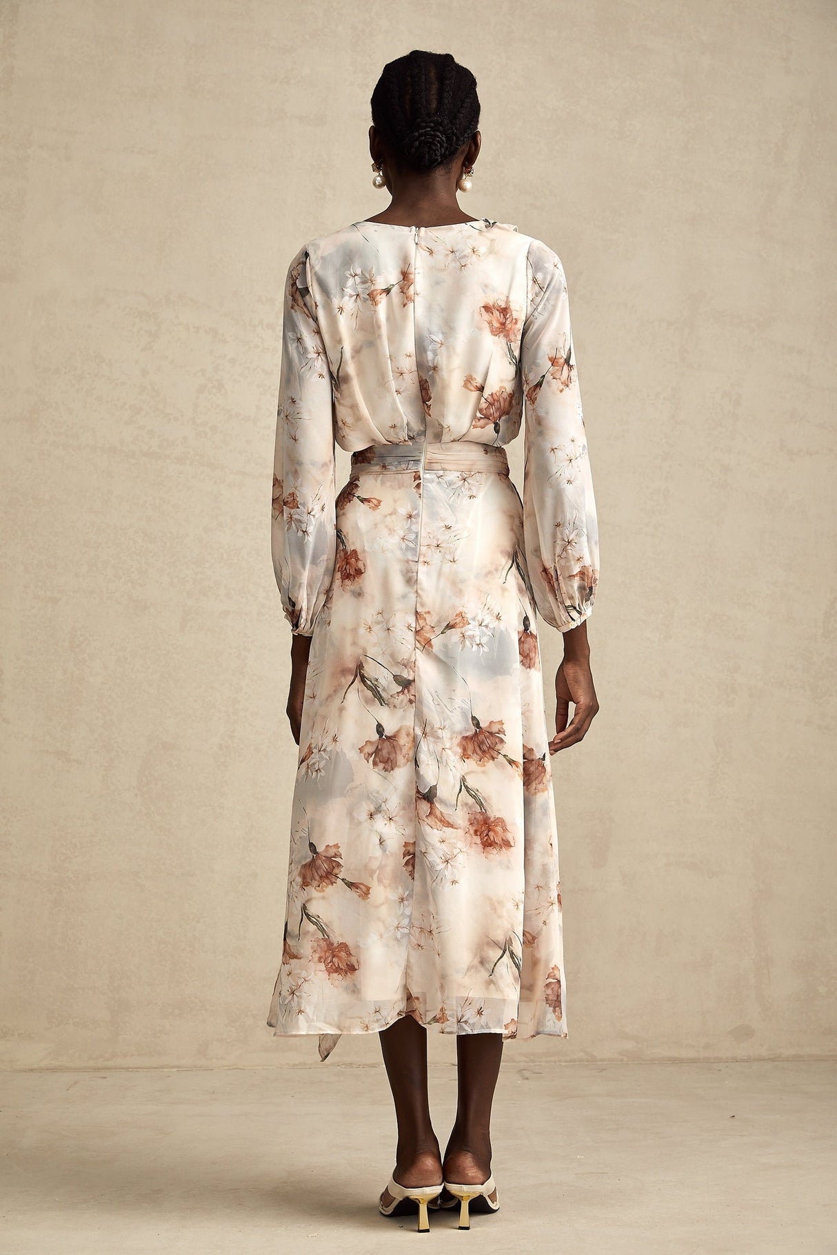 A woman wearing a floral print midi dress with an open waist design The dress has a colorful floral pattern on a light background It features long sleeves and a flowing skirt that falls to mid calf length The open waist detail adds a stylish and flattering touch to the silhouette
