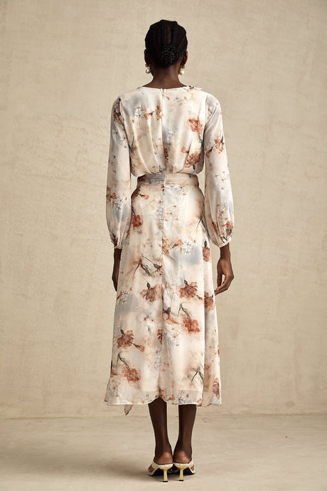 A woman wearing a floral print midi dress with an open waist design The dress has a colorful floral pattern on a light background It features long sleeves and a flowing skirt that falls to mid calf length The open waist detail adds a stylish and flattering touch to the silhouette