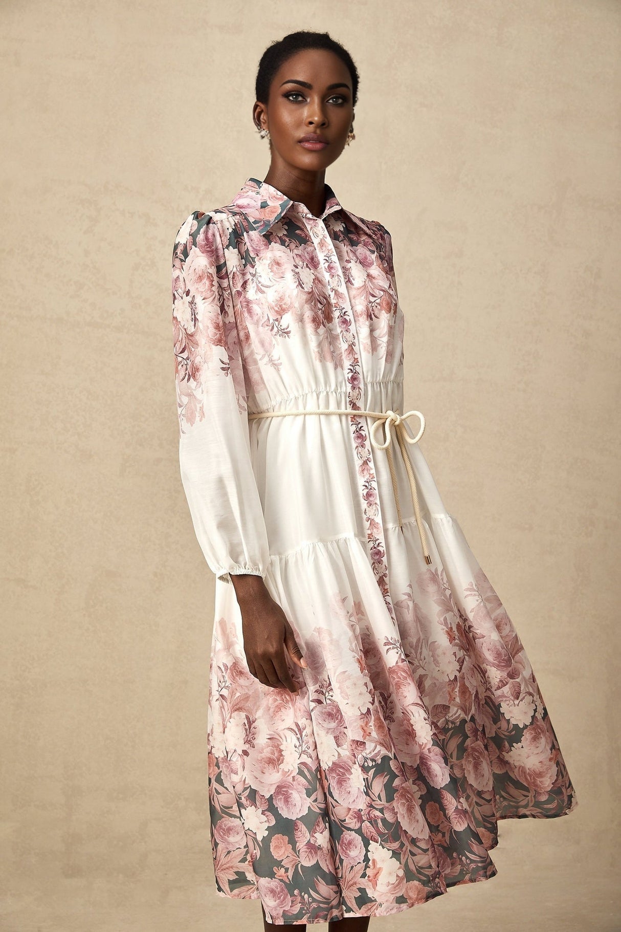A woman wearing a floral print midi dress with lantern sleeves standing in a relaxed pose against a plain background The dress features a colorful floral pattern on a light background and has a fitted bodice with a flowing skirt
