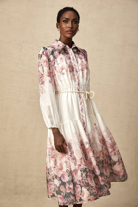 A woman wearing a floral print midi dress with lantern sleeves standing in a relaxed pose against a plain background The dress features a colorful floral pattern on a light background and has a fitted bodice with a flowing skirt