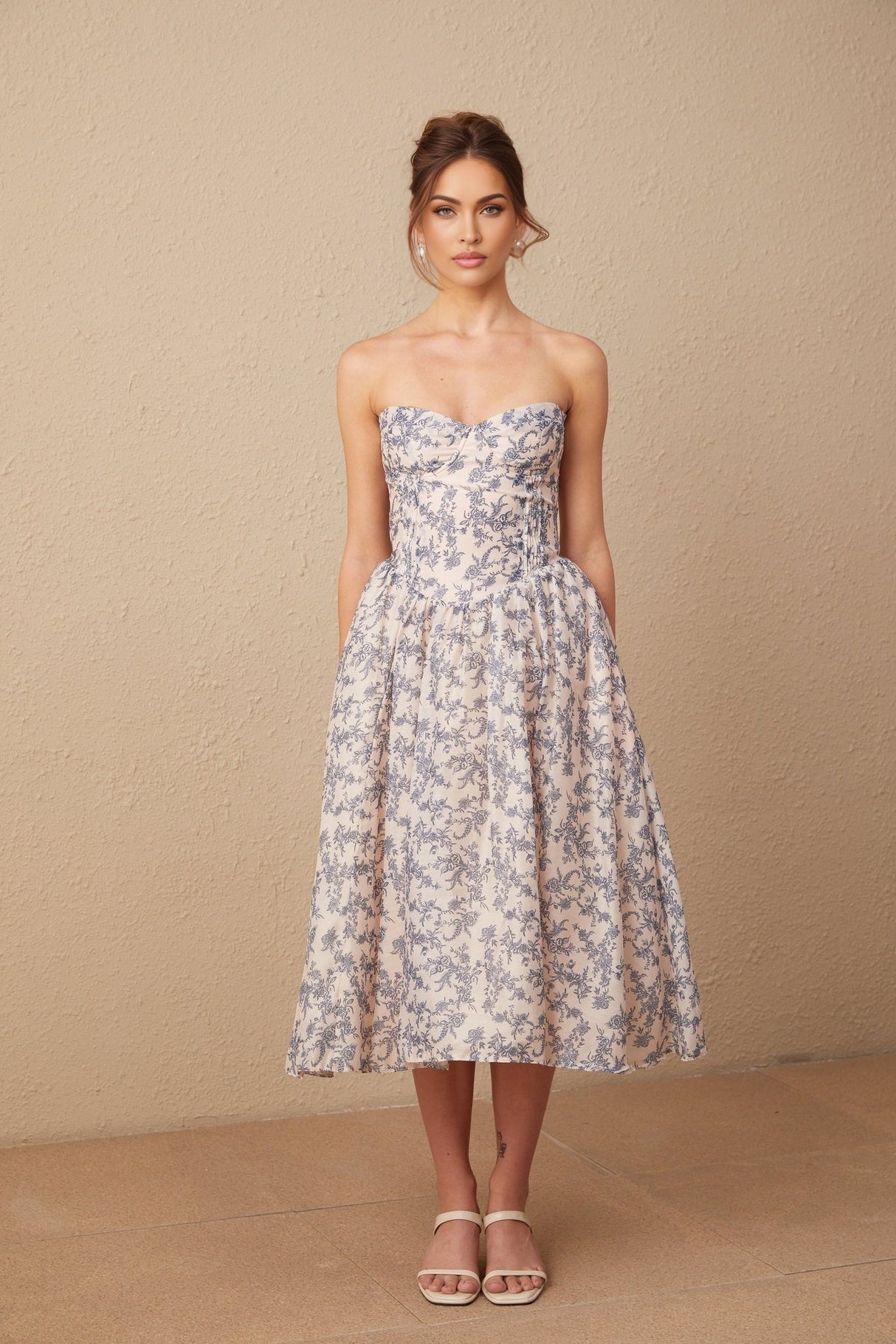 A woman wearing a floral print off shoulder midi dress with a fanny silhouette standing against a plain background