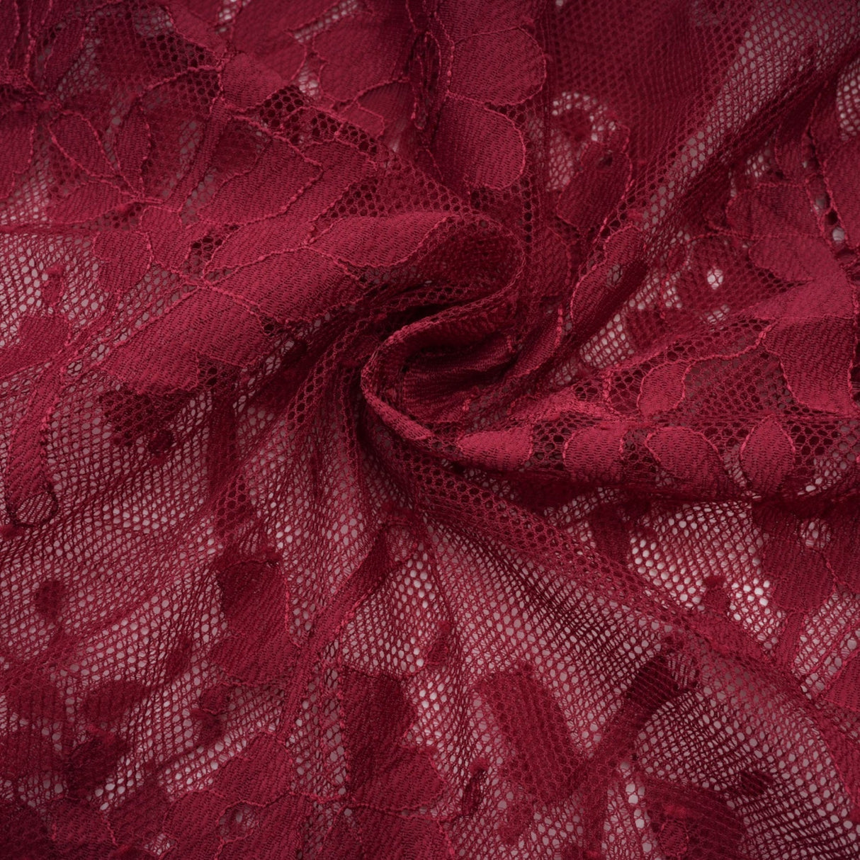 A woman wearing a flowing red lace dress with an oversized fit standing against a plain background