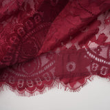 A woman wearing a flowing red lace dress with oversized fit standing against a plain background