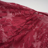 A woman wearing a flowing red oversize dress made of delicate chantilly lace posing against a plain background