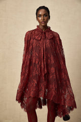 A woman wearing a flowing red oversize dress made of delicate chantilly lace standing against a plain background