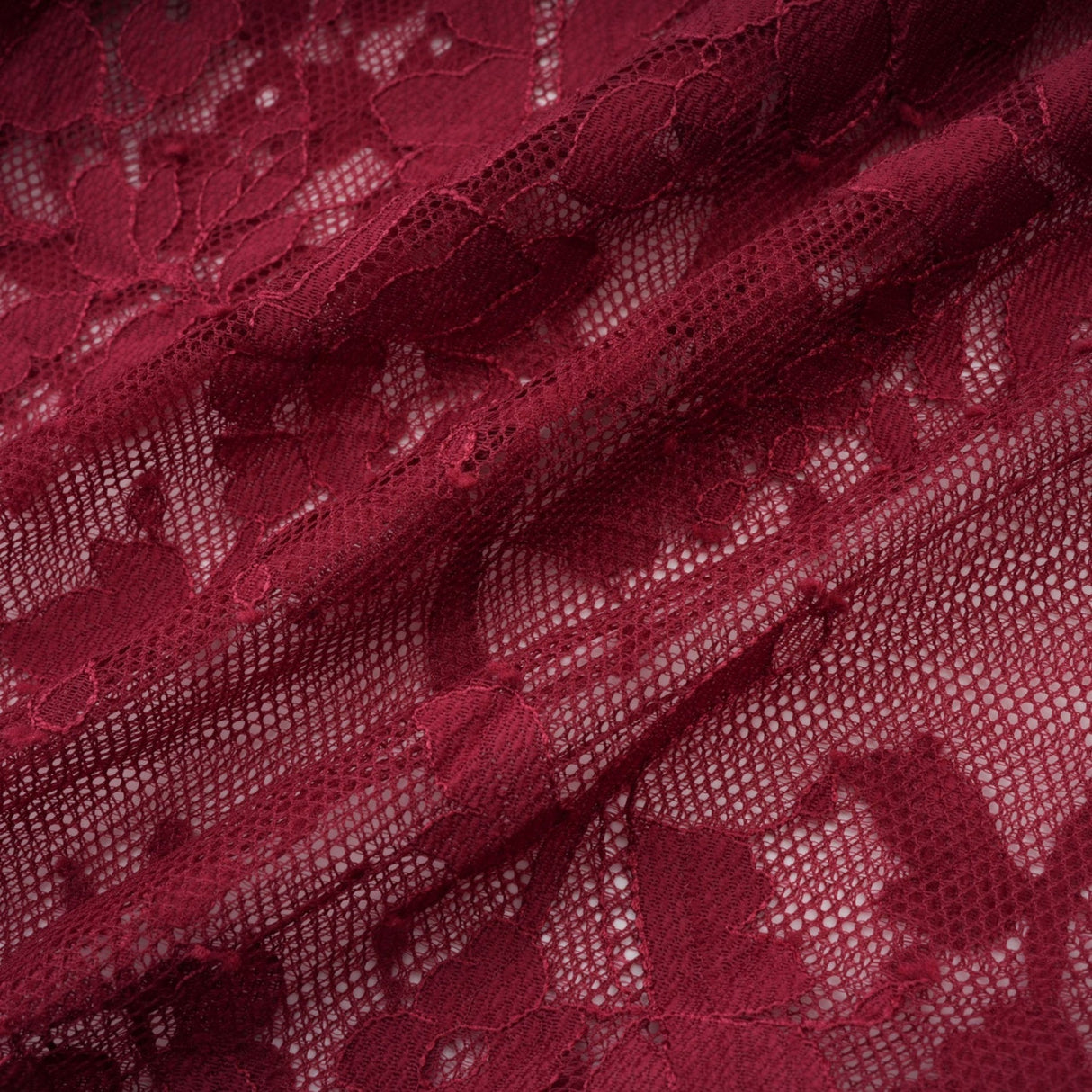 A woman wearing a flowing red oversize dress made of delicate chantilly lace standing in a neutral background