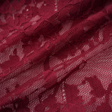 A woman wearing a flowing red oversize dress made of delicate chantilly lace standing in a neutral background