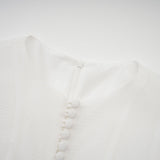 A woman wearing a flowy semi sheer mini dress with flared sleeves and a loose silhouette standing against a plain background