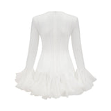 A woman wearing a flowy semi sheer white mini dress with flared sleeves and a loose fit standing against a plain background