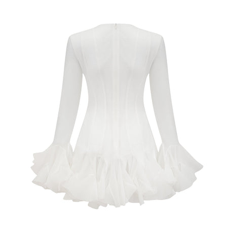 A woman wearing a flowy semi sheer white mini dress with flared sleeves and a loose fit standing against a plain background