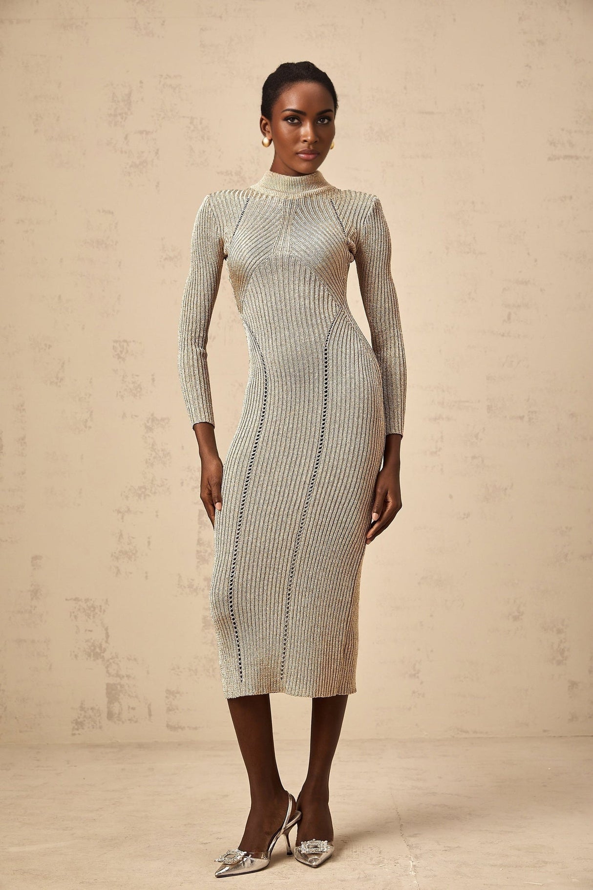 A woman wearing a gold ribbed knit midi dress with delicate pointelle details standing in a relaxed pose