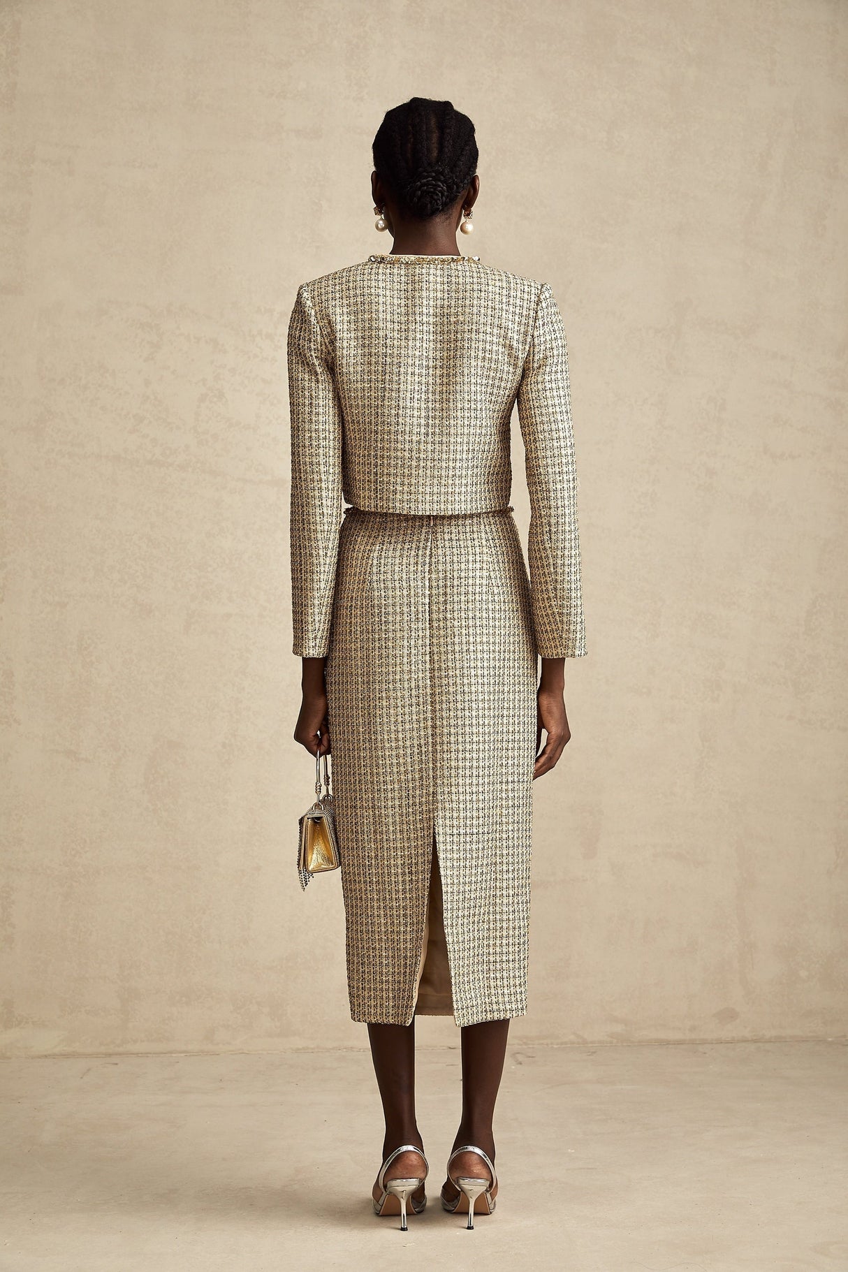 A woman wearing a gold tweed jacket and matching skirt set adorned with sequins The outfit has a luxurious and sparkling appearance suitable for formal or evening events