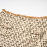 A woman wearing a gold tweed jacket and matching skirt set with sequin embellishments The outfit shimmers in the light and has a luxurious texture