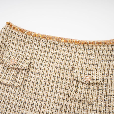A woman wearing a gold tweed jacket and matching skirt set with sequin embellishments The outfit shimmers in the light and has a luxurious texture