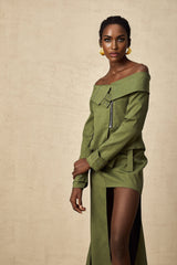 A woman wearing a green asymmetric jacket paired with a matching skirt standing against a plain background
