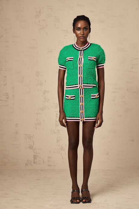 A woman wearing a green knitted matching set consisting of a sleeveless top and midi skirt standing against a neutral background