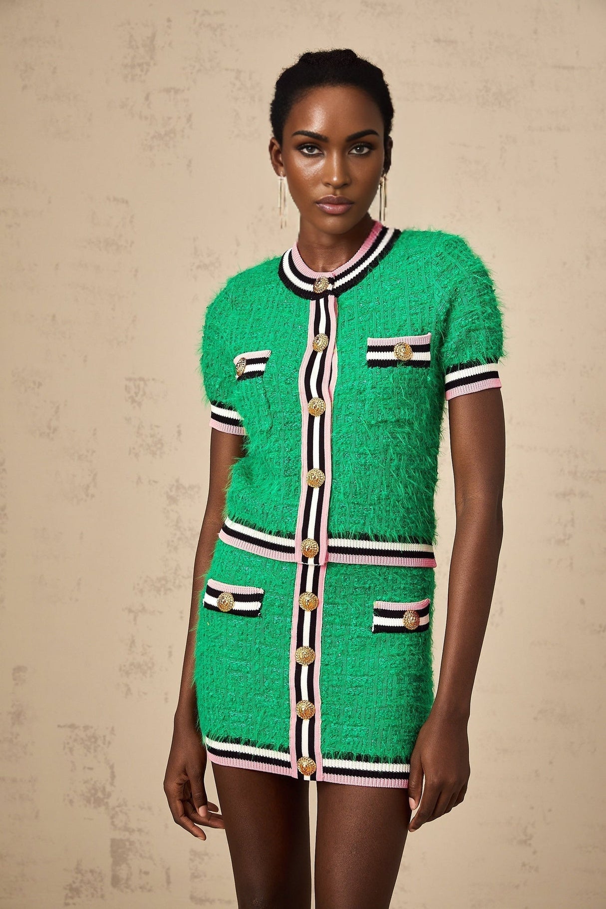 A woman wearing a green knitted matching set consisting of a top and skirt standing against a plain background