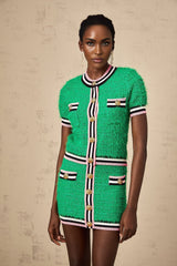 A woman wearing a green knitted matching set consisting of a top and skirt standing against a plain background
