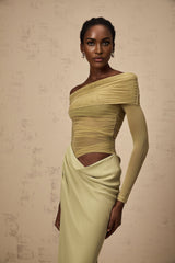 A woman wearing a green offshoulder midi dress with semisheer fabric standing in a relaxed pose