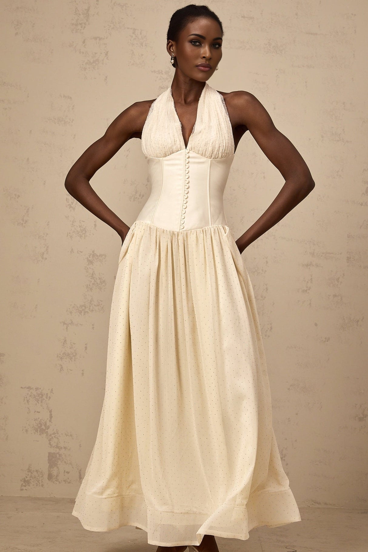 A woman wearing a halterneck tulle midi dress in a soft shade standing against a plain background The dress features a fitted bodice and flowy skirt with delicate tulle layers