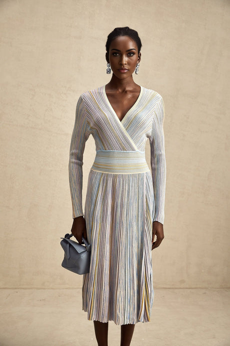 A woman wearing a kneelength knitted dress with vertical stripes standing in a relaxed pose the dress has a fitted silhouette and long sleeves showcasing the Amelie design