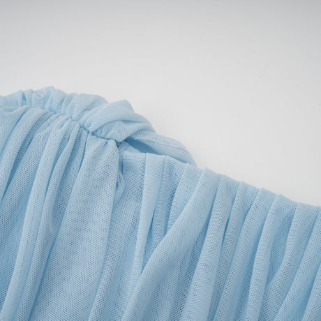 A woman wearing a light blue asymmetric pleated maxi dress with a flowing skirt and one shoulder design