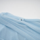 A woman wearing a light blue asymmetric pleated maxi dress with a flowing skirt and one shoulder design