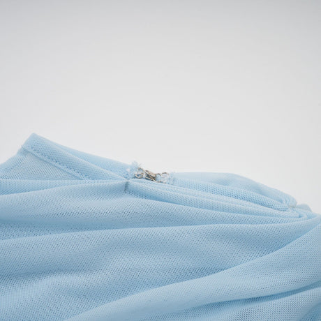 A woman wearing a light blue asymmetric pleated maxi dress with a flowing skirt and one shoulder strap