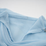 A woman wearing a light blue asymmetric pleated maxi dress with a flowy silhouette and one shoulder strap