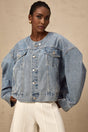 A woman wearing a light blue collarless denim jacket with front pockets and button closure